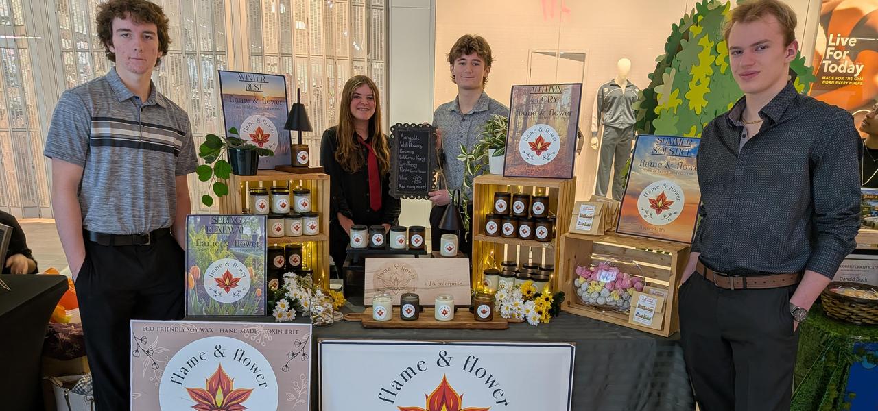 4 Students standing around a table filled with product and signage reading Flame and Flower.